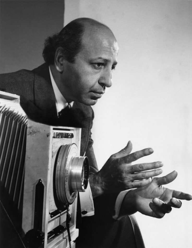 Black and white photograph of the photographer Yousuf Karsh, standing by a large format camera