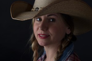 Head and shoulders photographic portrait of blonde model in plaits wearing cowboy hat