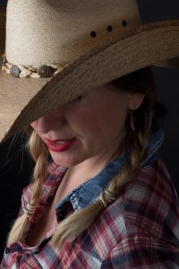 Head and shoulders photographic portrait of blonde model in plaits wearing cowboy hat