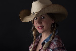 Head and shoulders photographic portrait of blonde model in plaits wearing cowboy hat