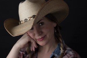 Head and shoulders photographic portrait of blonde model in plaits wearing cowboy hat