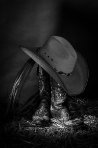 Black and white still life photograph of cowboy boots and hat