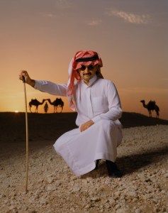 Colour photograph of Saudi Prince in desert, camels in the background, by Michael O'Neill